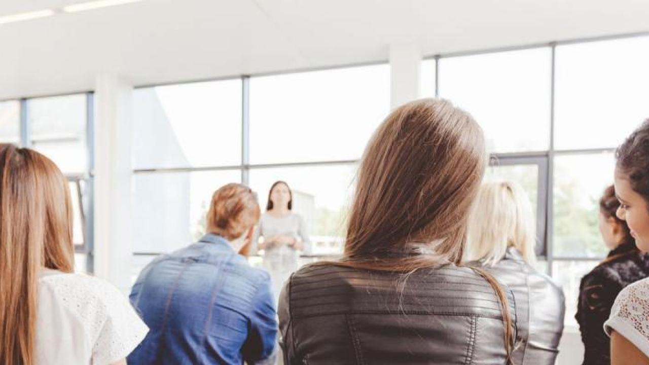 People sitting in a classroom in front of large, sunny windows