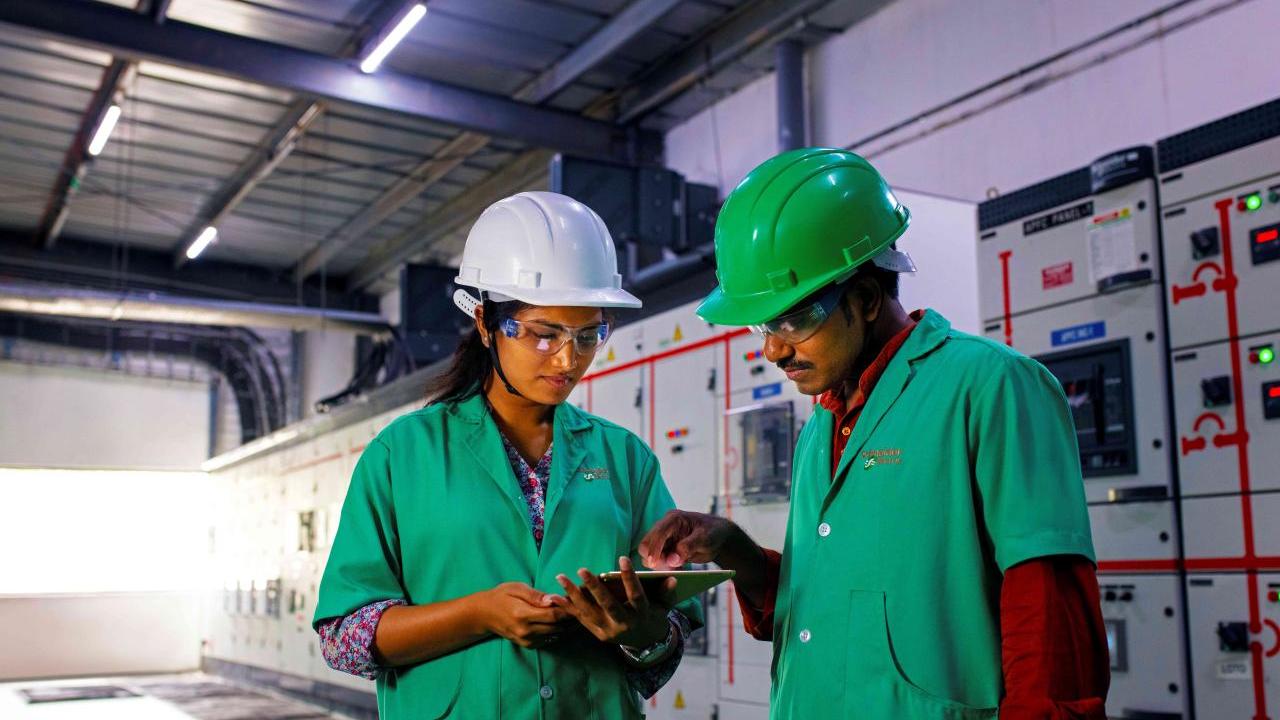 Two people in uniforms and hard hats, one pointing at a tablet being held by the other.