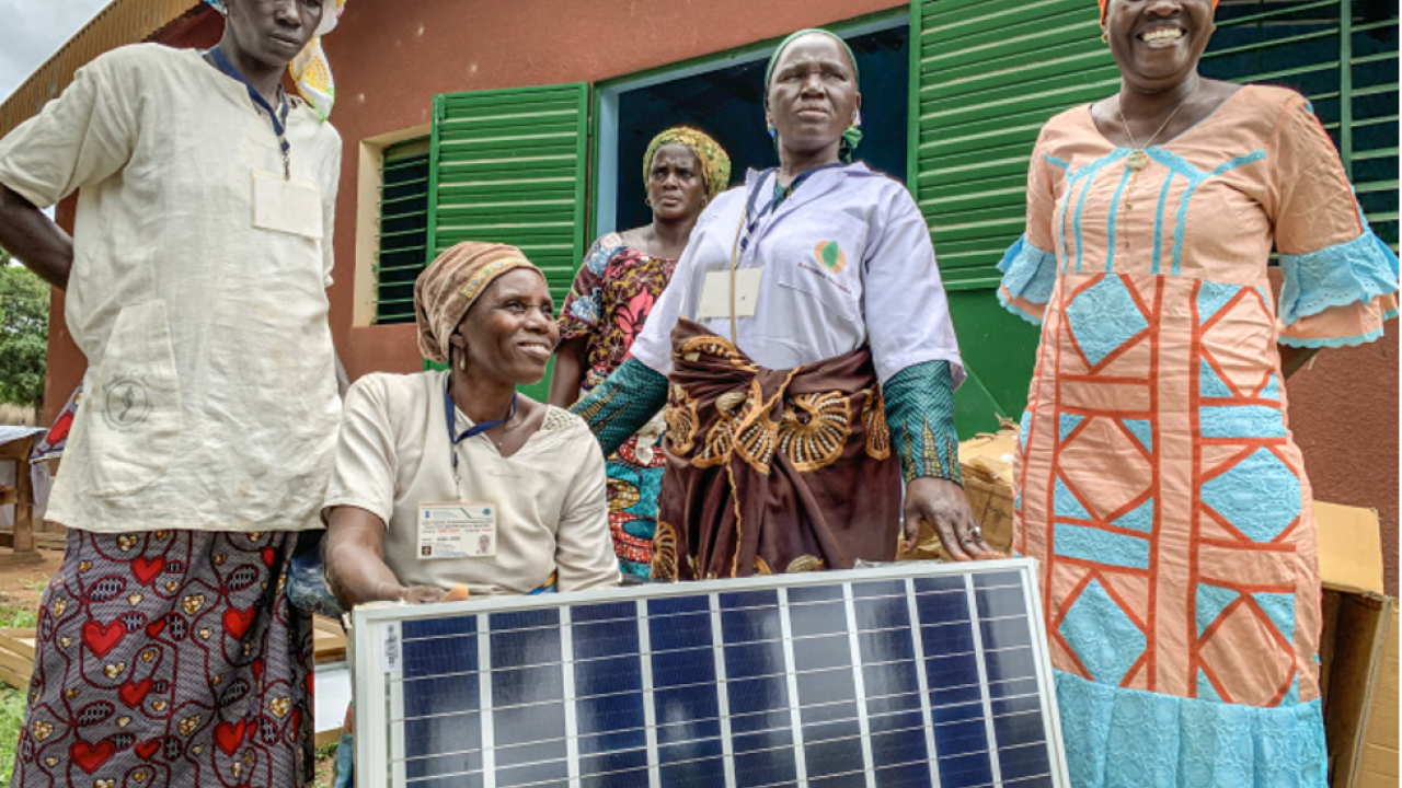 Villagers in bright clothes pose with a solar panel