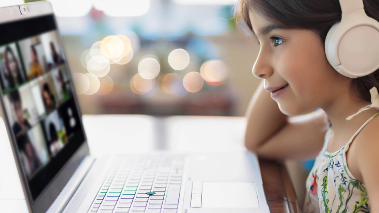 smiling child wearing headphones while looking at a laptop screen