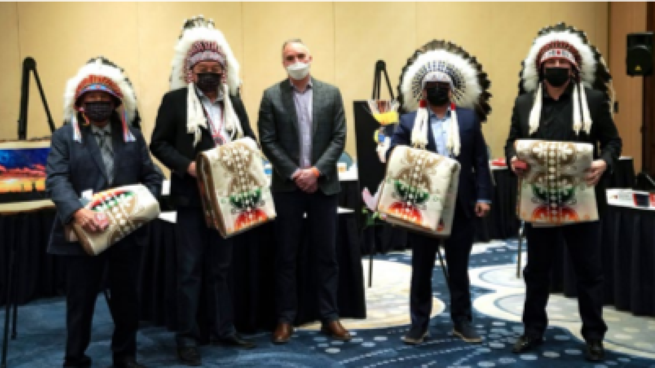 a group of five people, four wearing native american head coverings and carry woven blankets