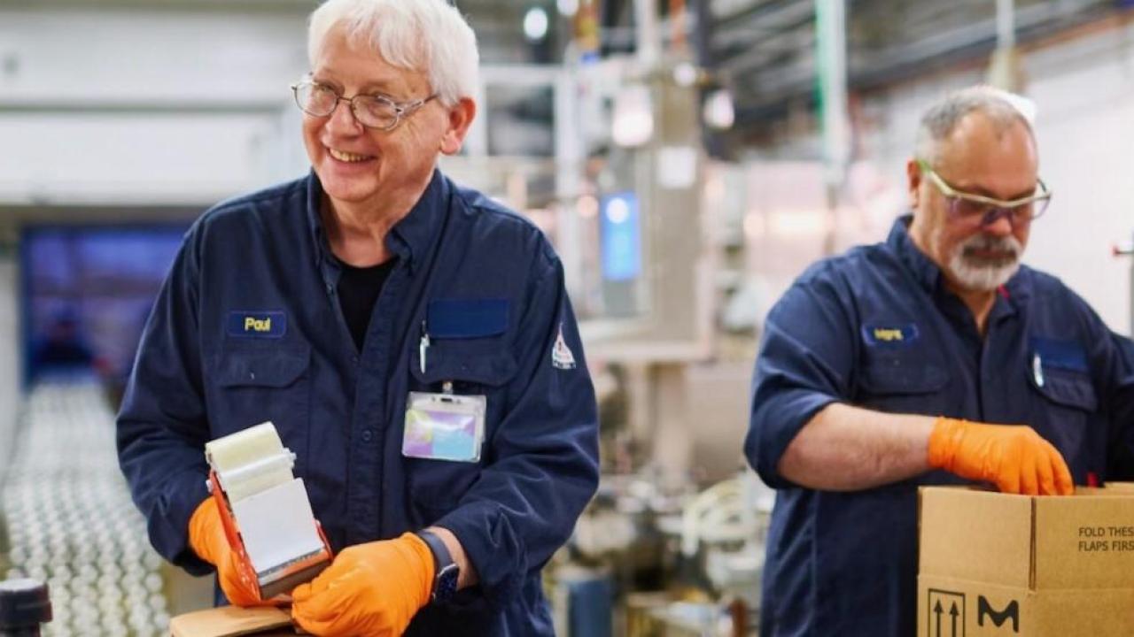 Two workers packaging products into boxes at a facility.