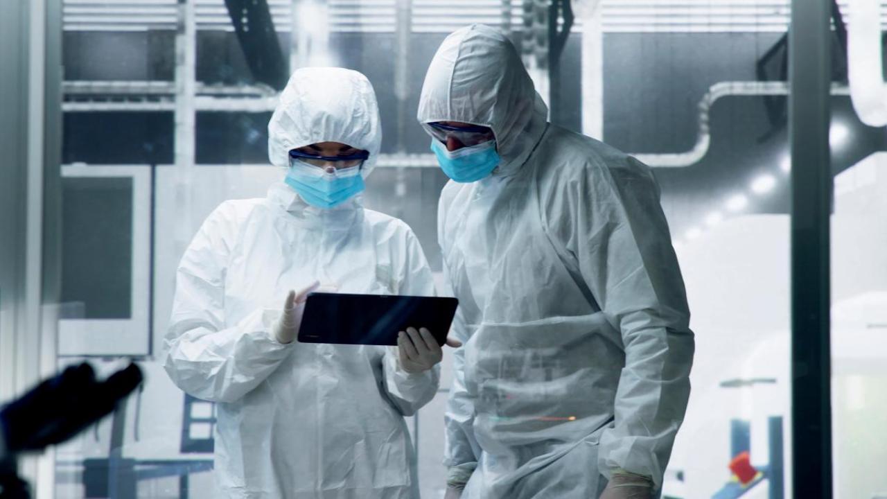 Two people in protective clothing looking at a tablet