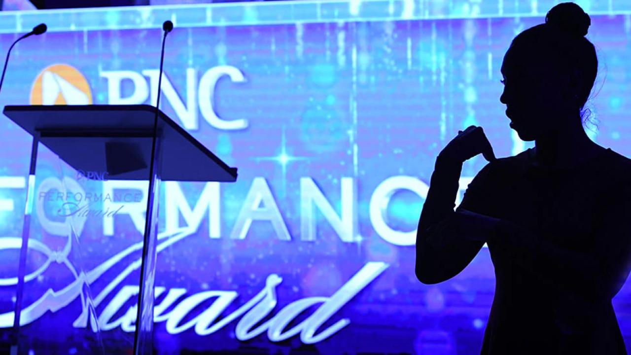 "PNC Performance Awards" projected on a large screen behind a podium. A person in shadow beside it.