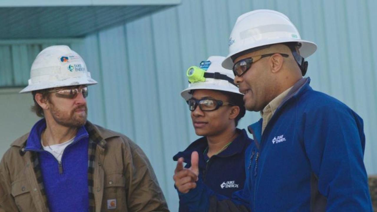 Derrick Smith with two others in hard hats, talking outside a building.