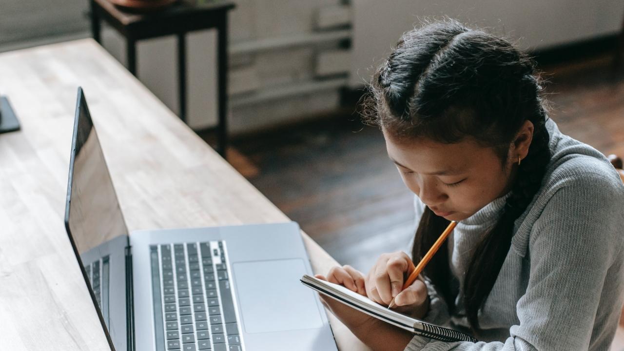 girl with laptop writing in notebook