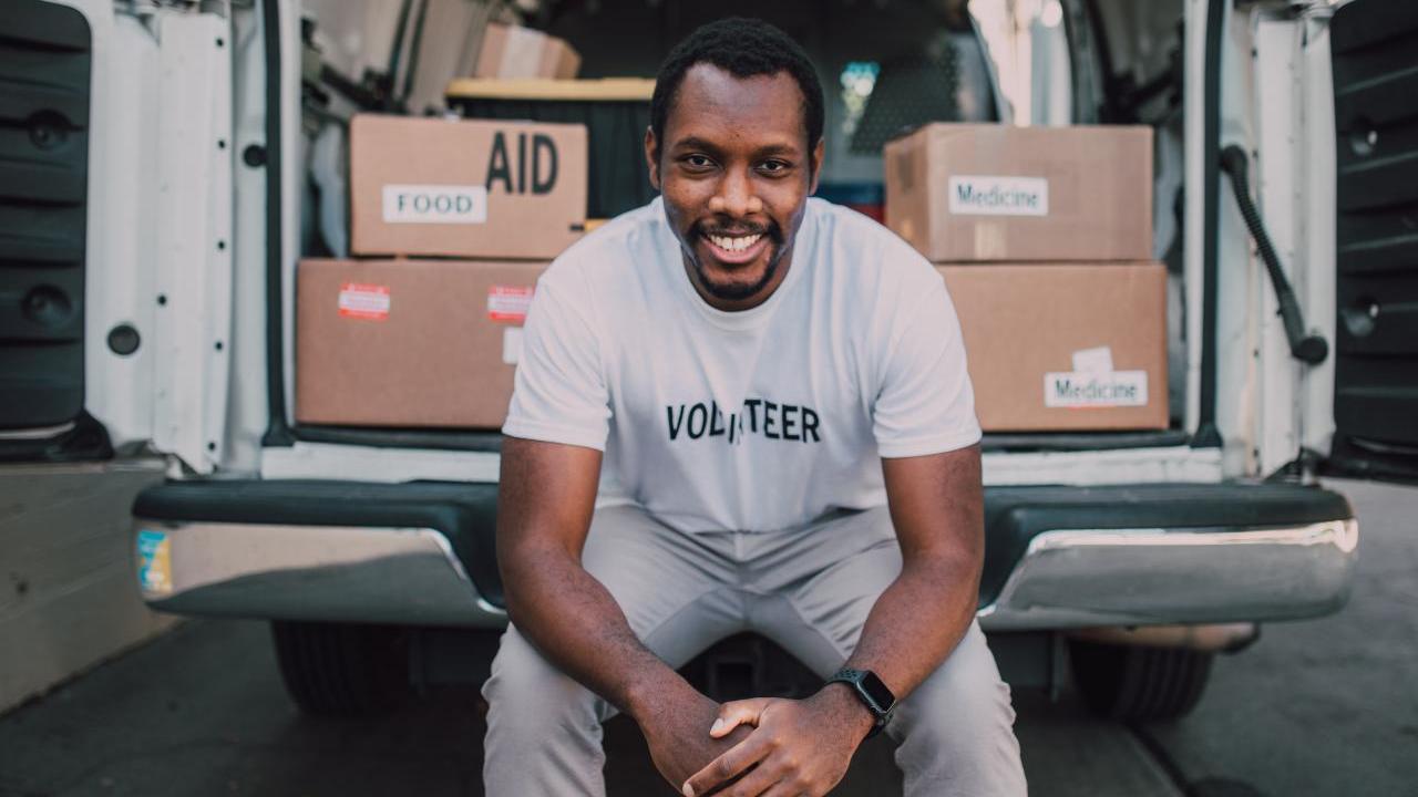 Volunteer man sitting in the open bay of a van filled with boxes and supplies.