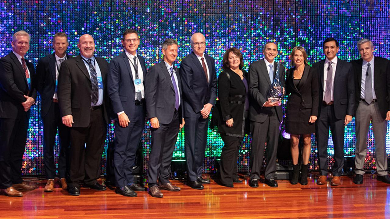 Group of people in a row on a stage. One holding an award.