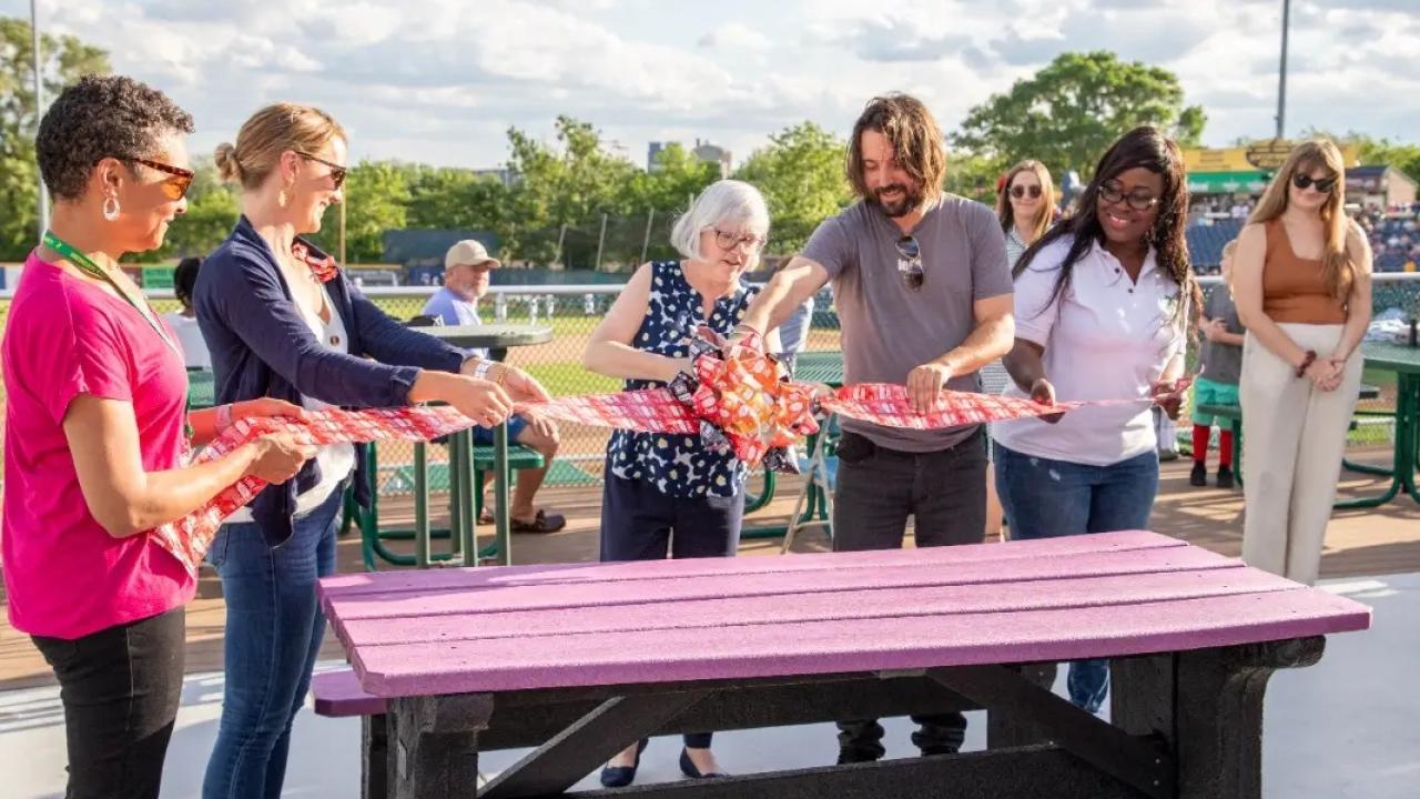a group of people cut a ribbon over a picnic table outside