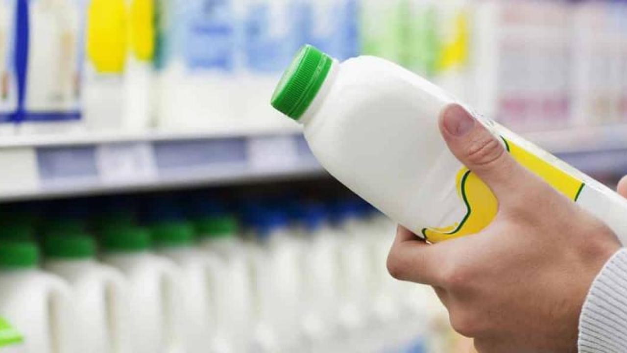 A person in a grocery store looking at a plastic container full of white liquid.