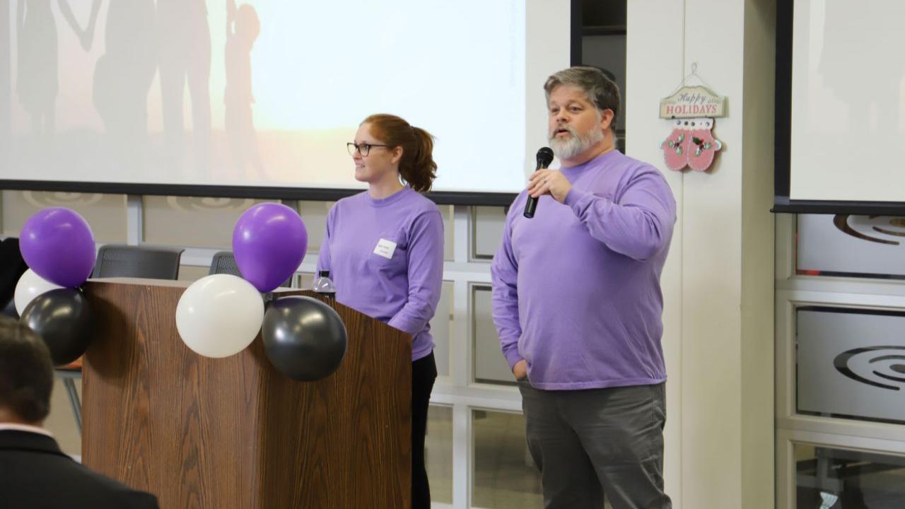 Two people in matching purple shirts behind a podium.