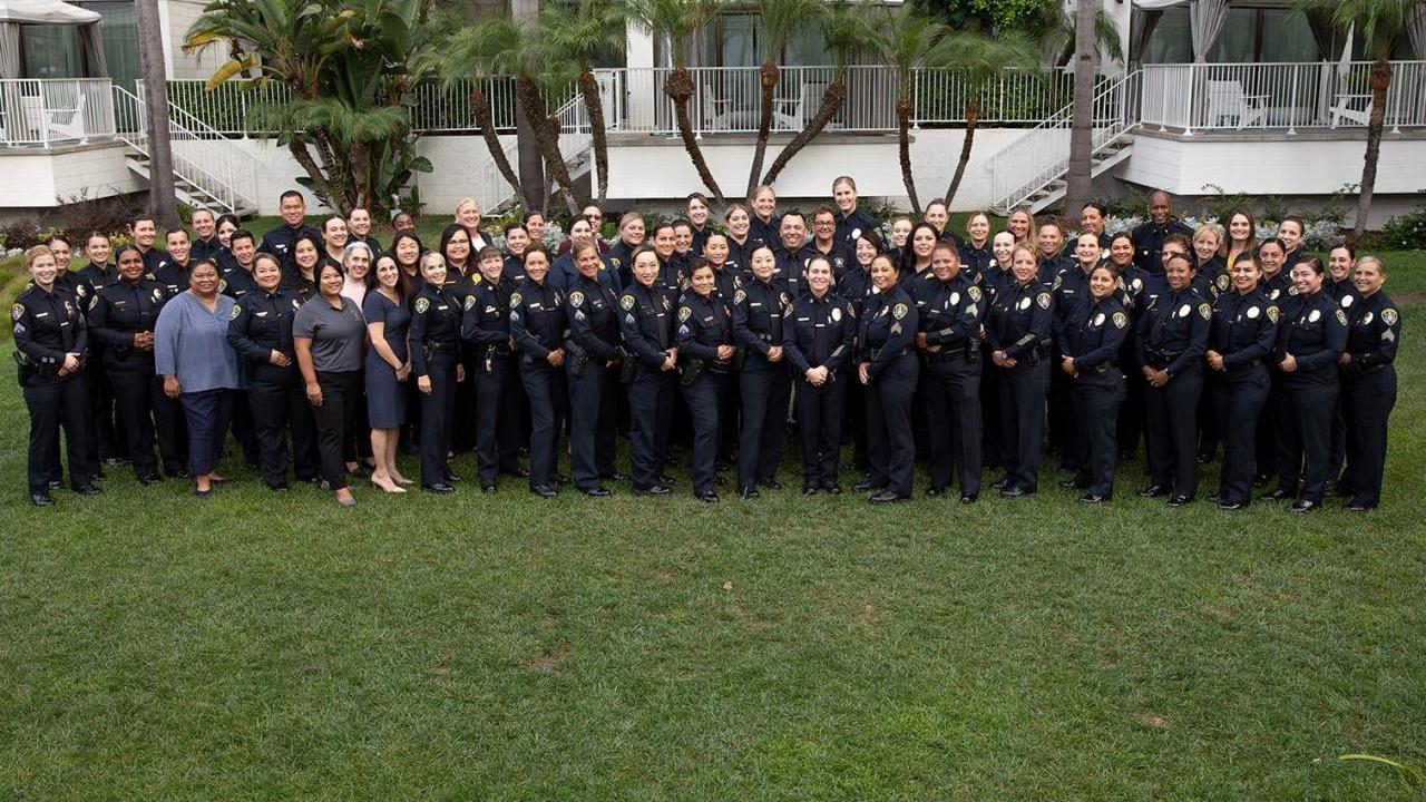 A large group of police officers in uniform and others posed in a grassy area.