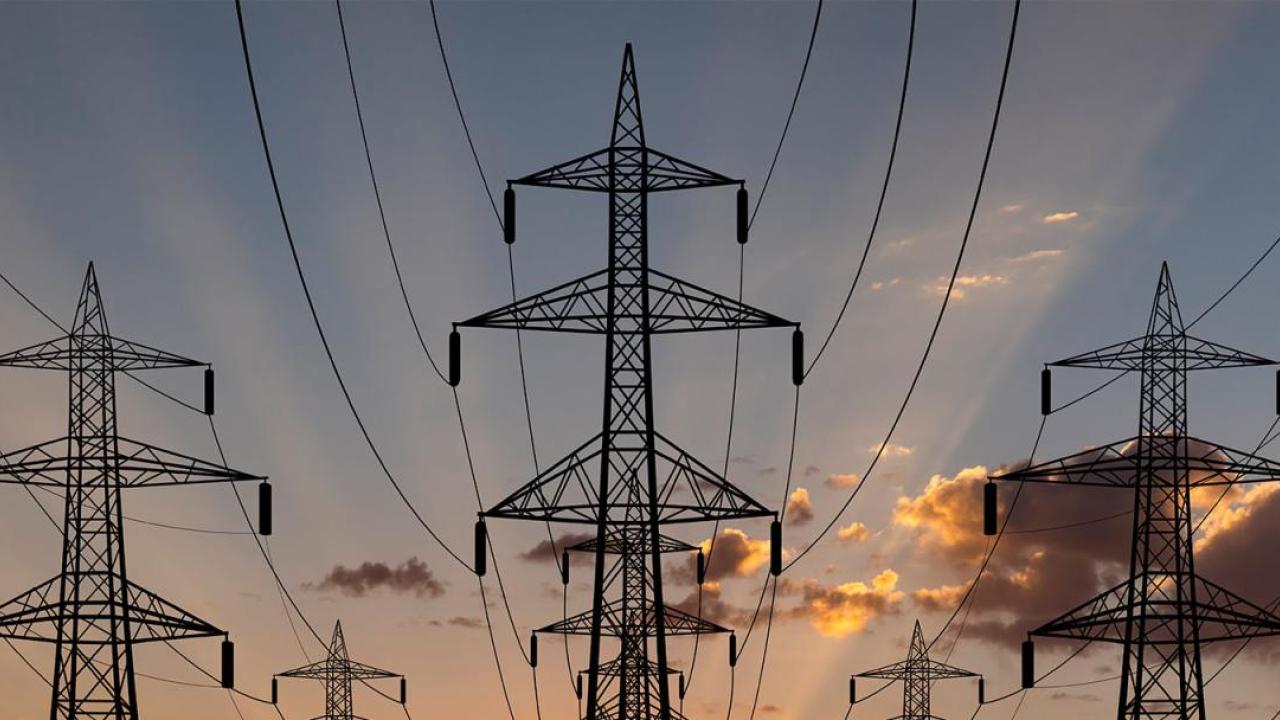 Tall electrical line towers, a setting sun behind them.