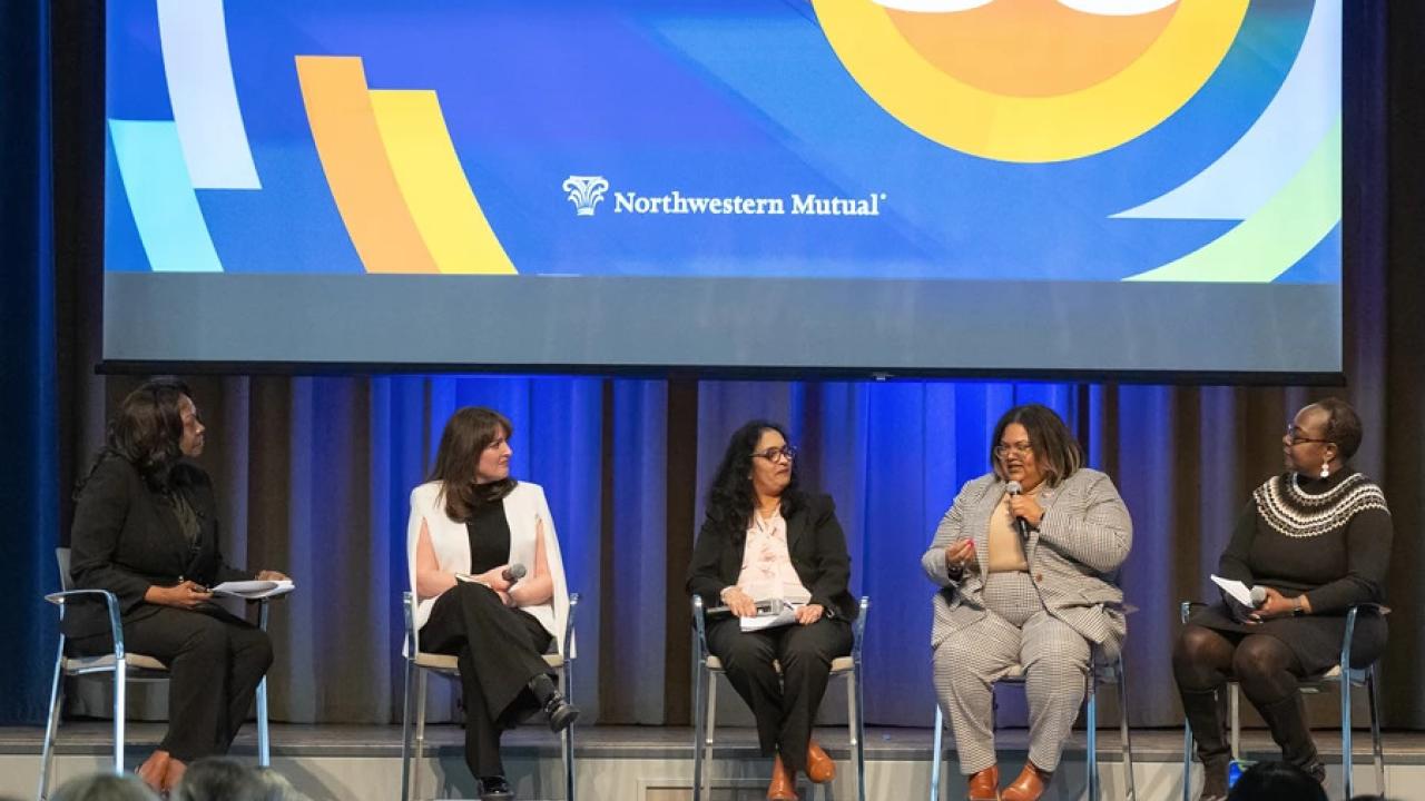 Five people with microphones seated on a stage in front of an audience.