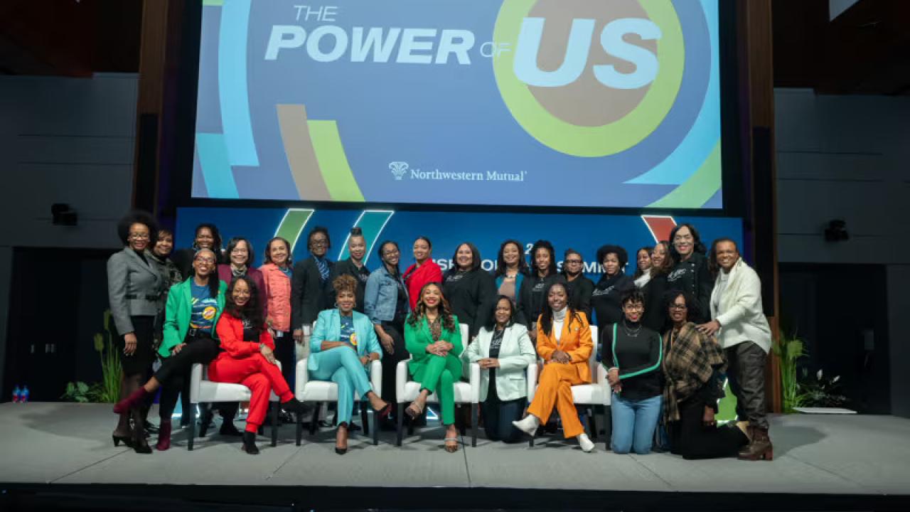 A group posed on a stage. "The Power of Us" displayed behind them.