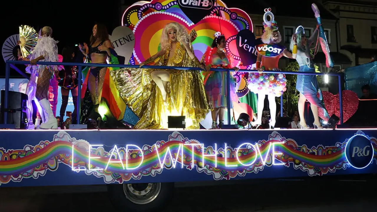 People riding on a pride float with glowing lights that read "Lead with love"