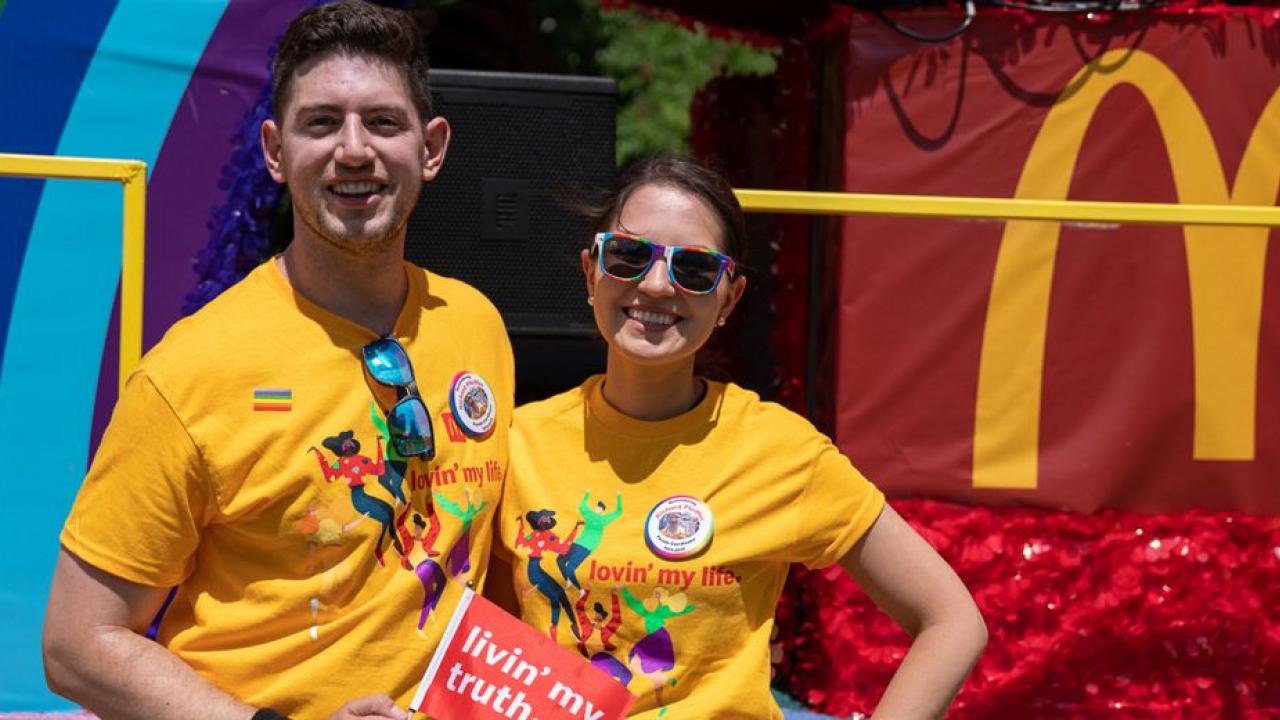 Two people in matching shirts. McDonalds logo and part of a rainbow behind them.