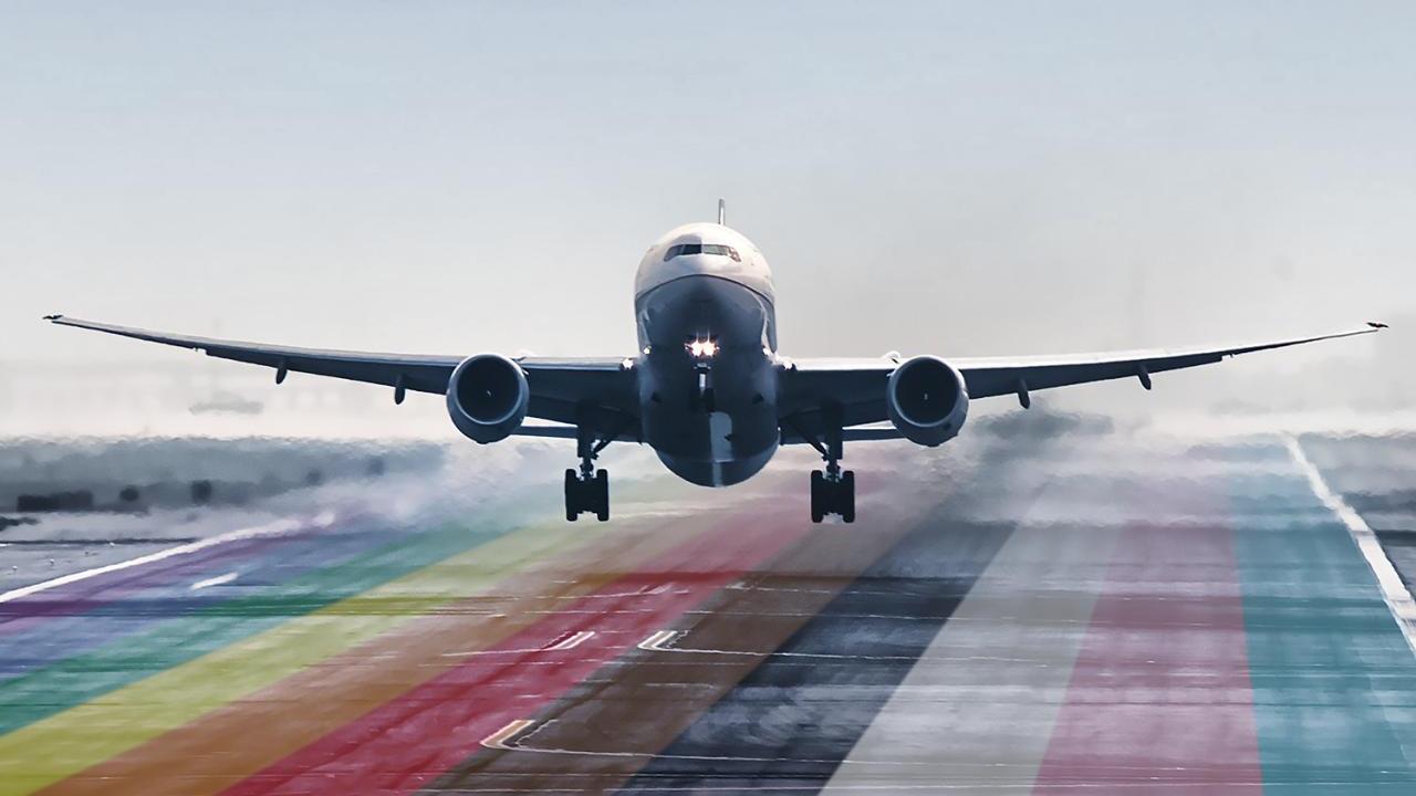 An airplane landing on a runway colored with LGBTQ+ flag colors