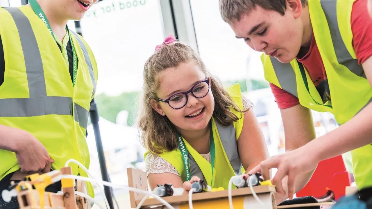 three children in high visibility vests work on an engineering project in a classroom