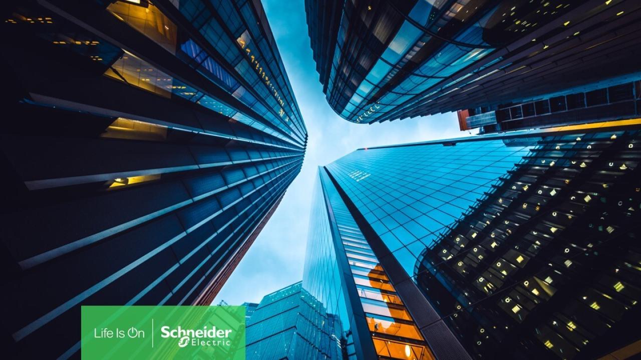 Looking up from the ground to the sky, surrounded by tall buildings close together. Schneider Electric logo at the bottom.