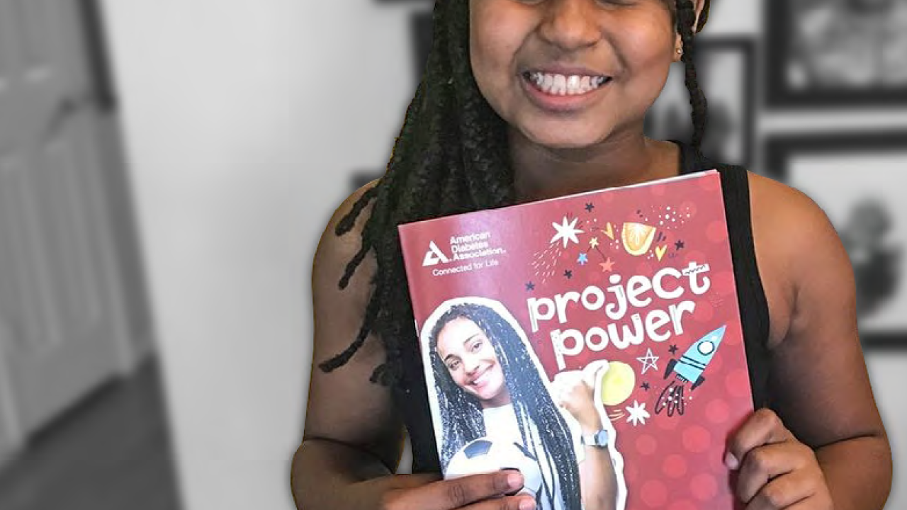 a child holds a book "project power" standing in front of a wall of family photos