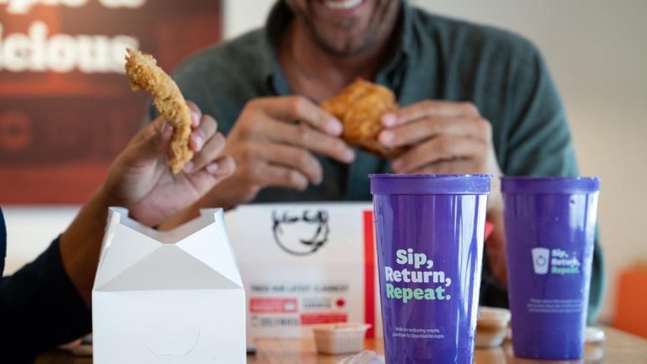 People eating chicken, purple cups in the foreground