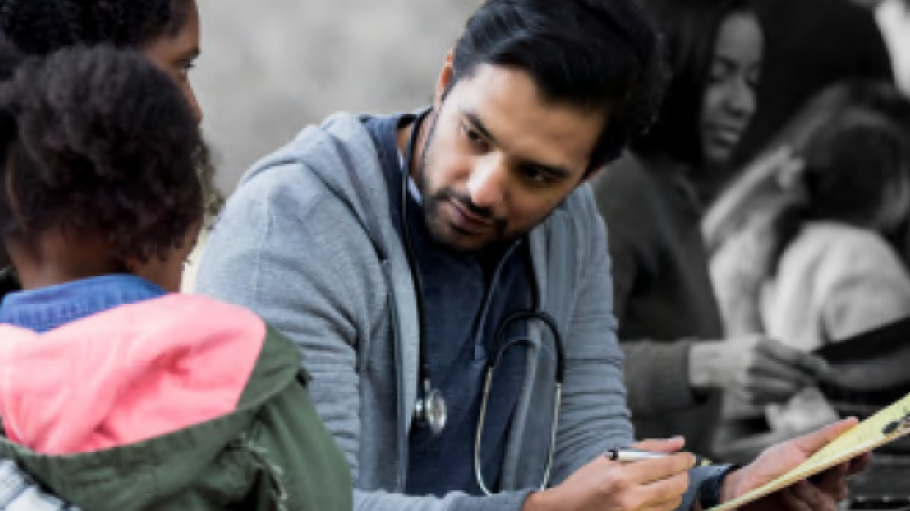a doctor sits writing on a clipboard, an adult and child on the left