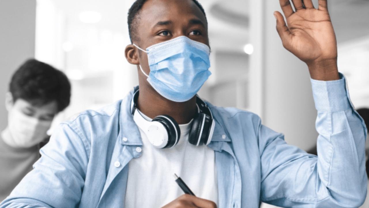 Black student in a blue shirt and mask raising their hand