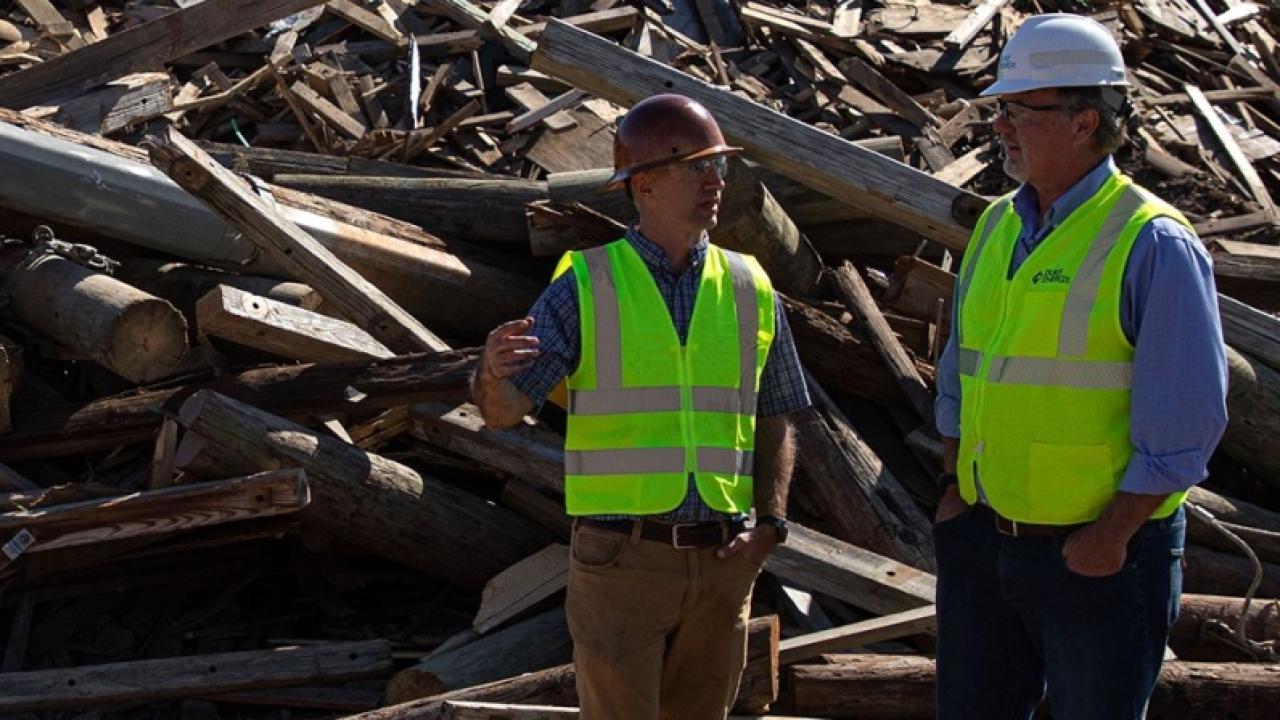 2 workers standing in front of a pile of old power poles