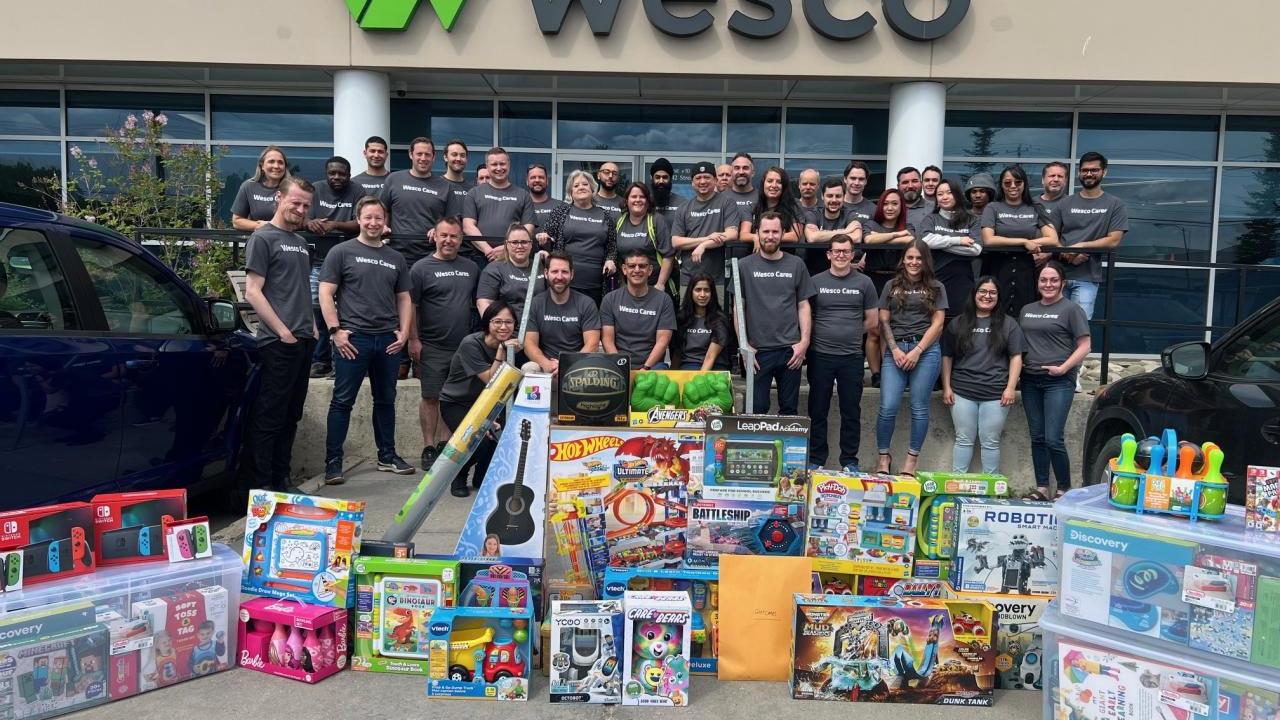 A group standing behind new toys, in front of a Wesco building