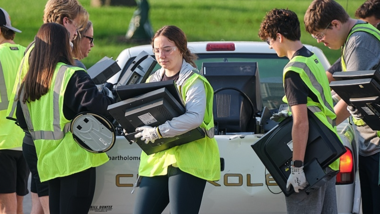 A group of people with safety vests, gloves, and glasses unload electronics from the back of a truck.