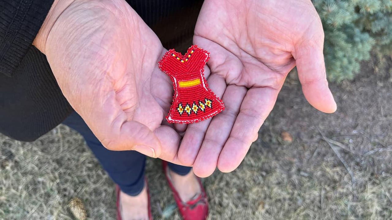 Hands holding a miniature red dress made of beads