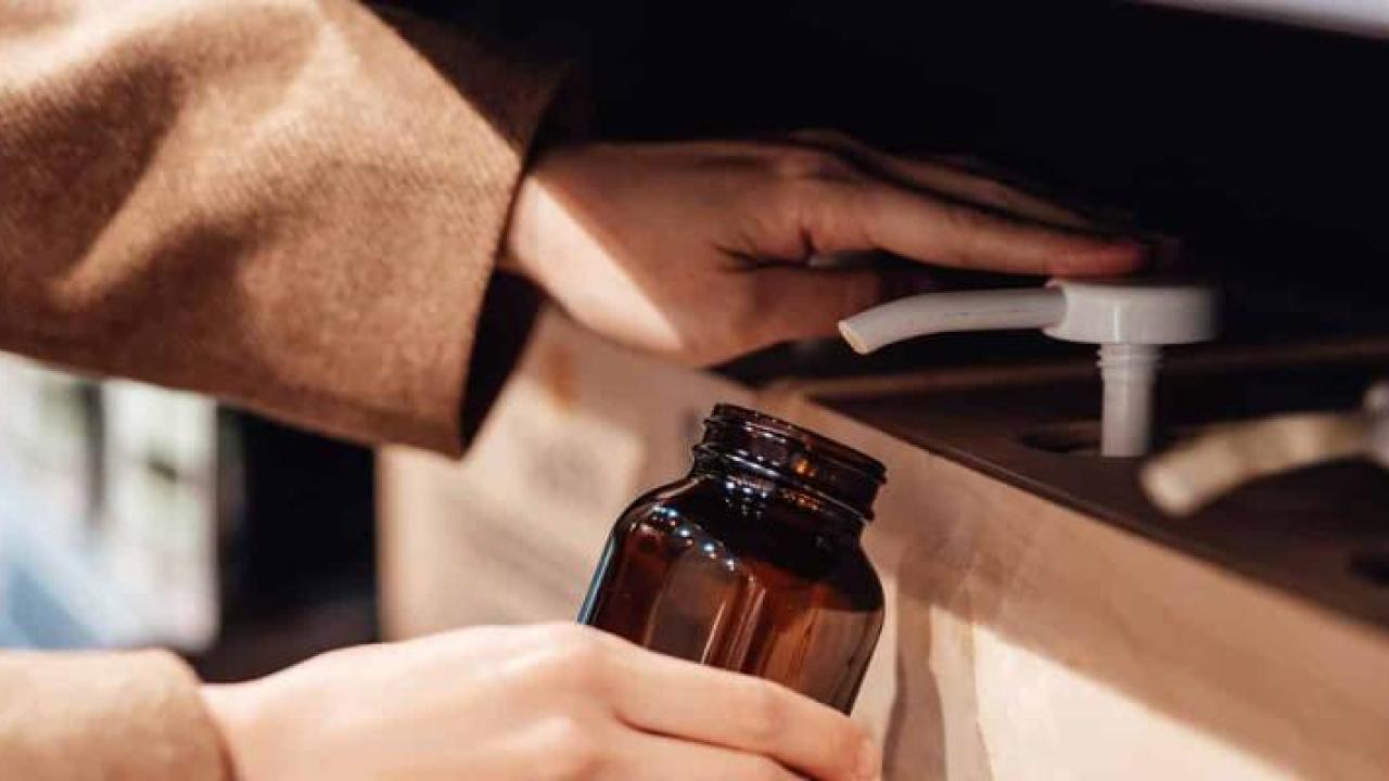 A person filling a brown glass jar from a row of pumps.