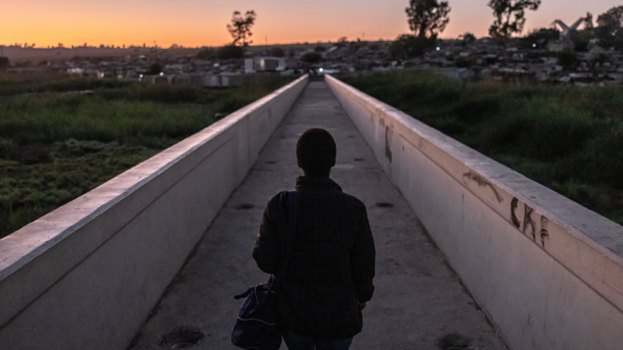 A silhouette of a person walking a narrow path towards houses in twilight.