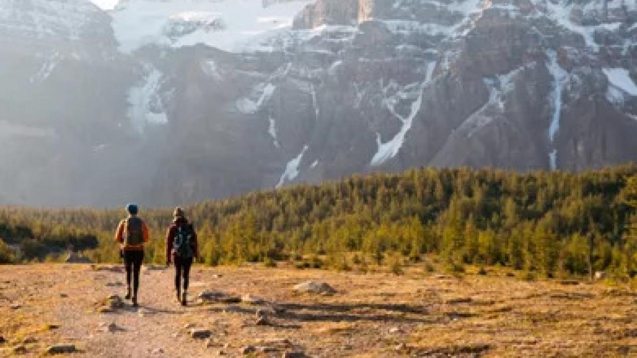 Two people walking away on a dirt path in a mountainous, scenic area.