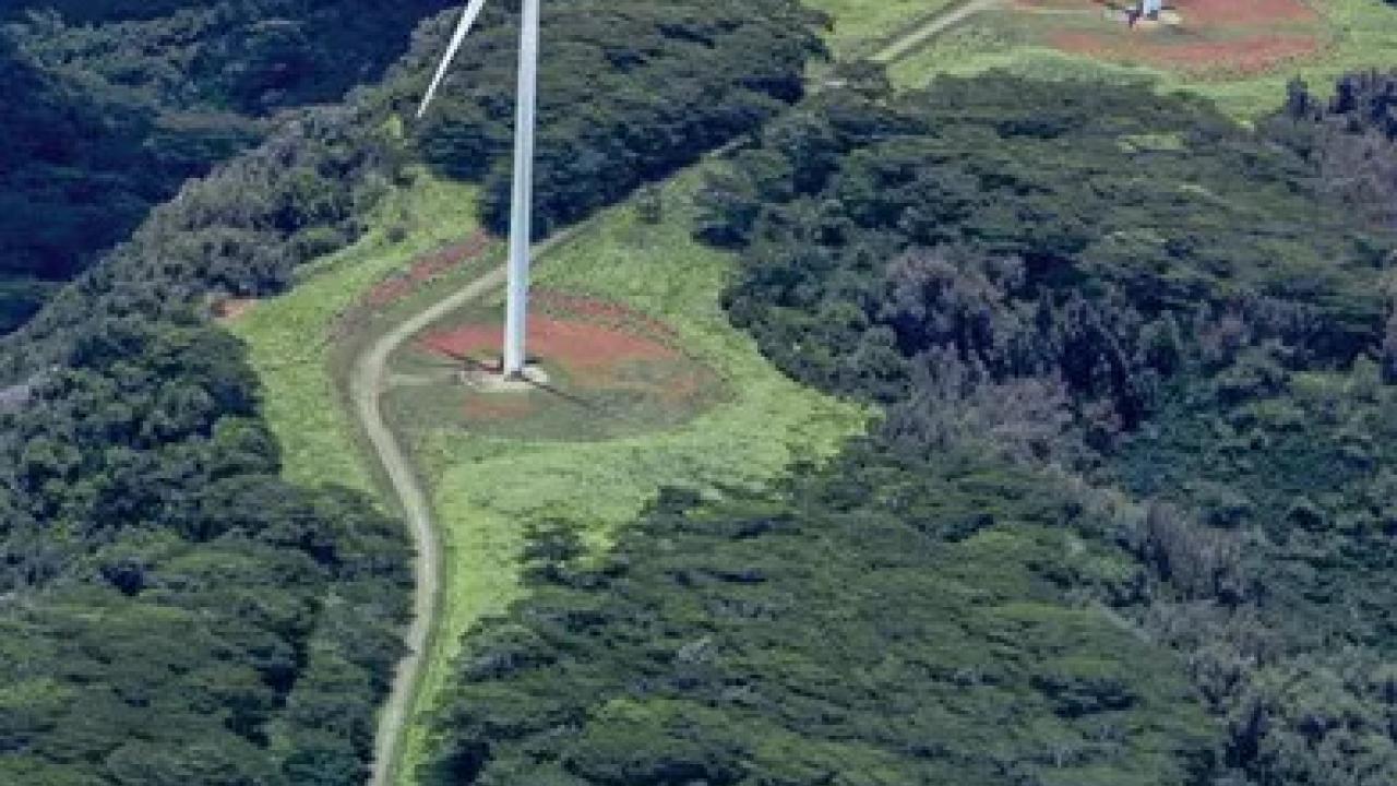 Aerial view of two wind turbines in a mountainous, tree-dense area.