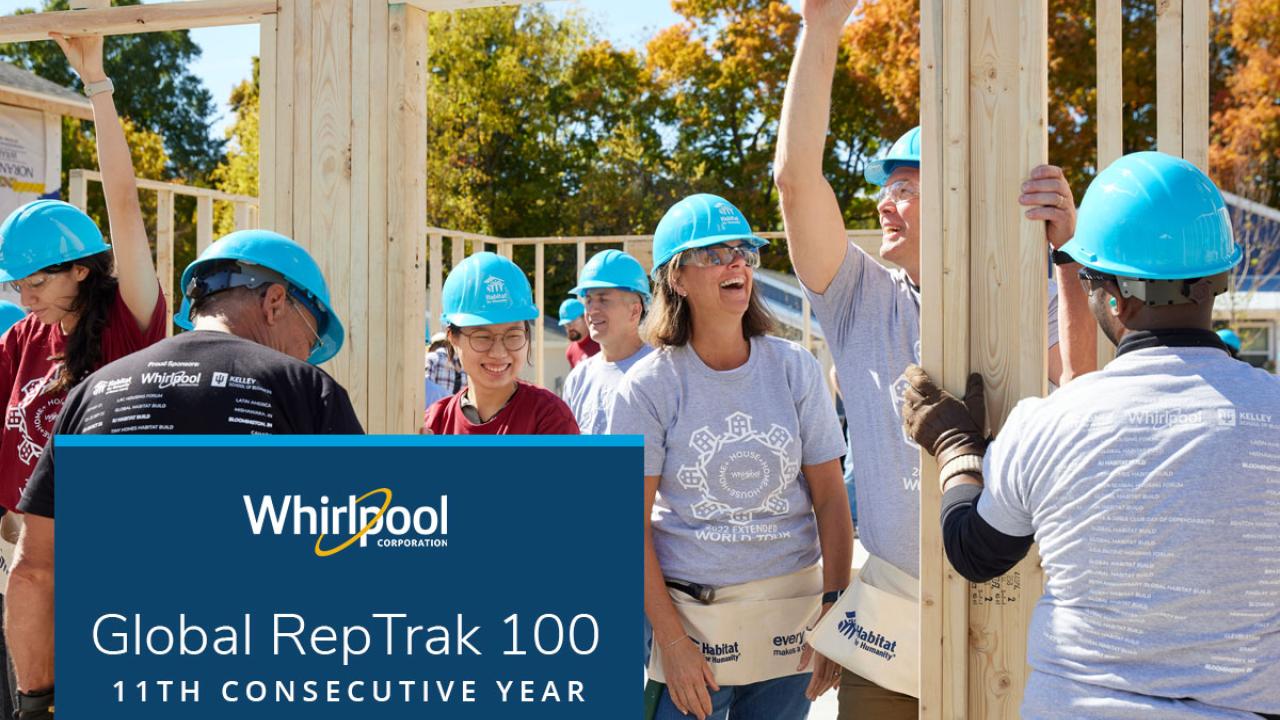 A group of people in matching blue hard hats, some holding wood framing on a construction site.