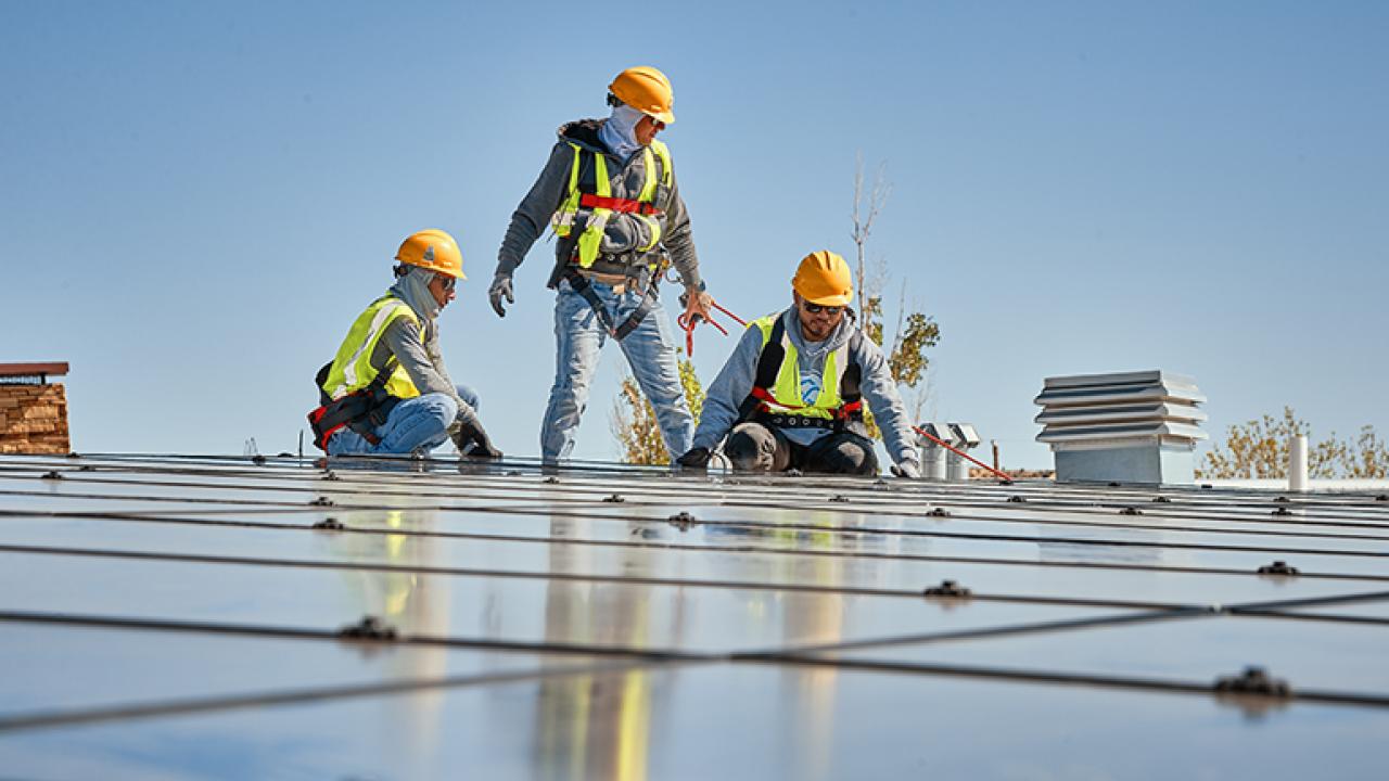 Three people in high-vis garments and hard hats installing solar panels.