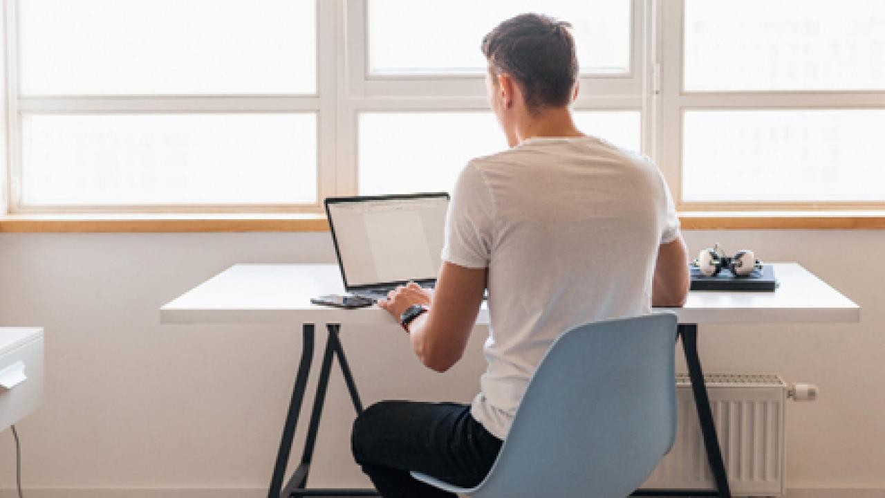 Person sitting at a desk with a laptop, in front of a bright window