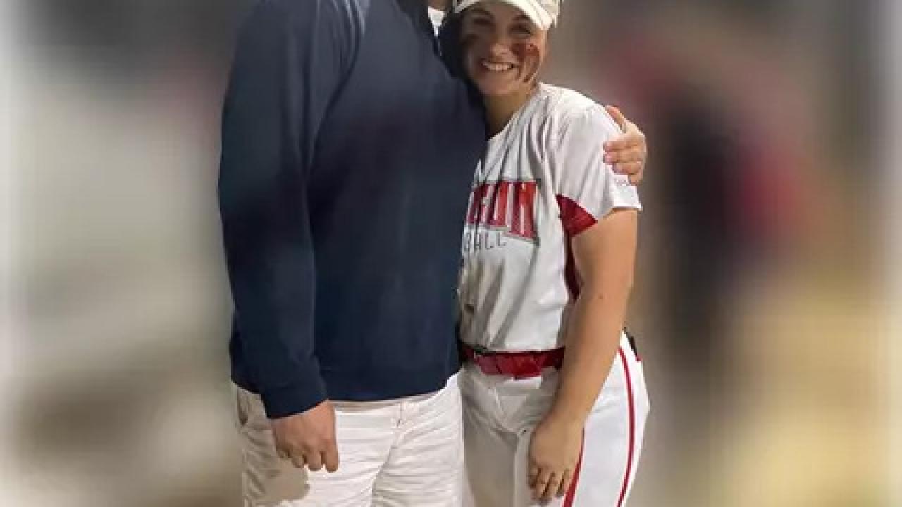 Two people posed, hugging. One in a baseball uniform.