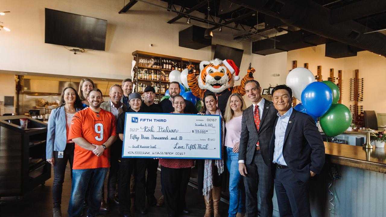 A group posed in a restaurant with a large check. A tiger mascot behind them.
