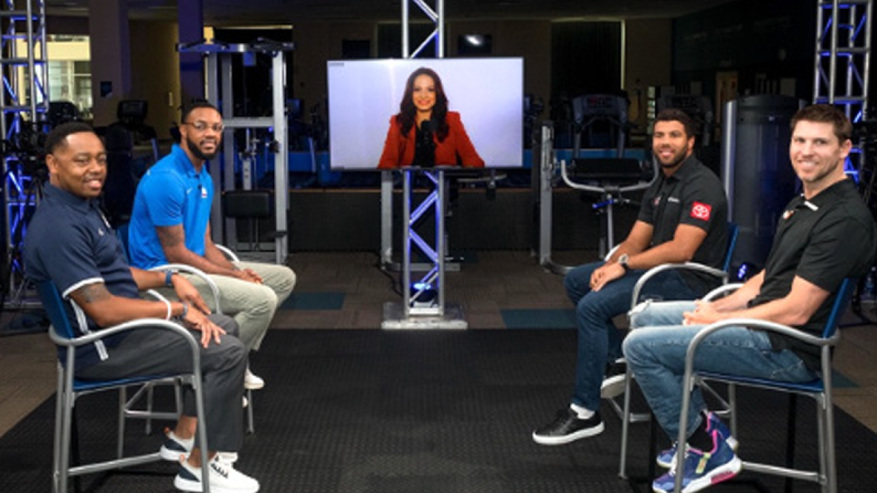 a group of four people an a person appearing on a monitor all seated in a studio