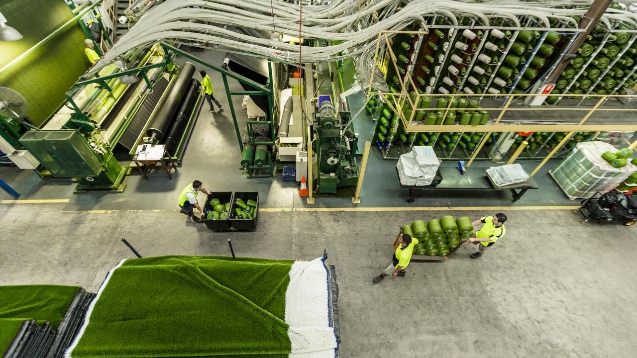 factory workers in safety gear stack and move bins of green plastic
