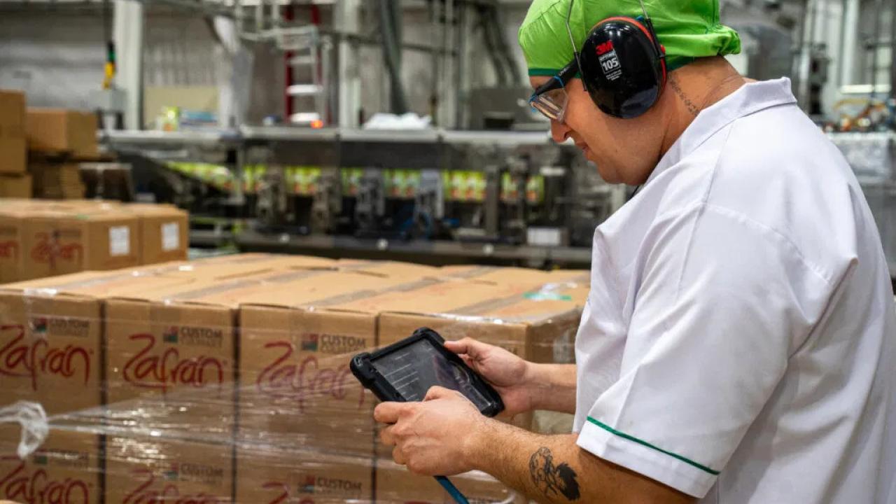 A person with ear protection using a tablet in a warehouse setting.