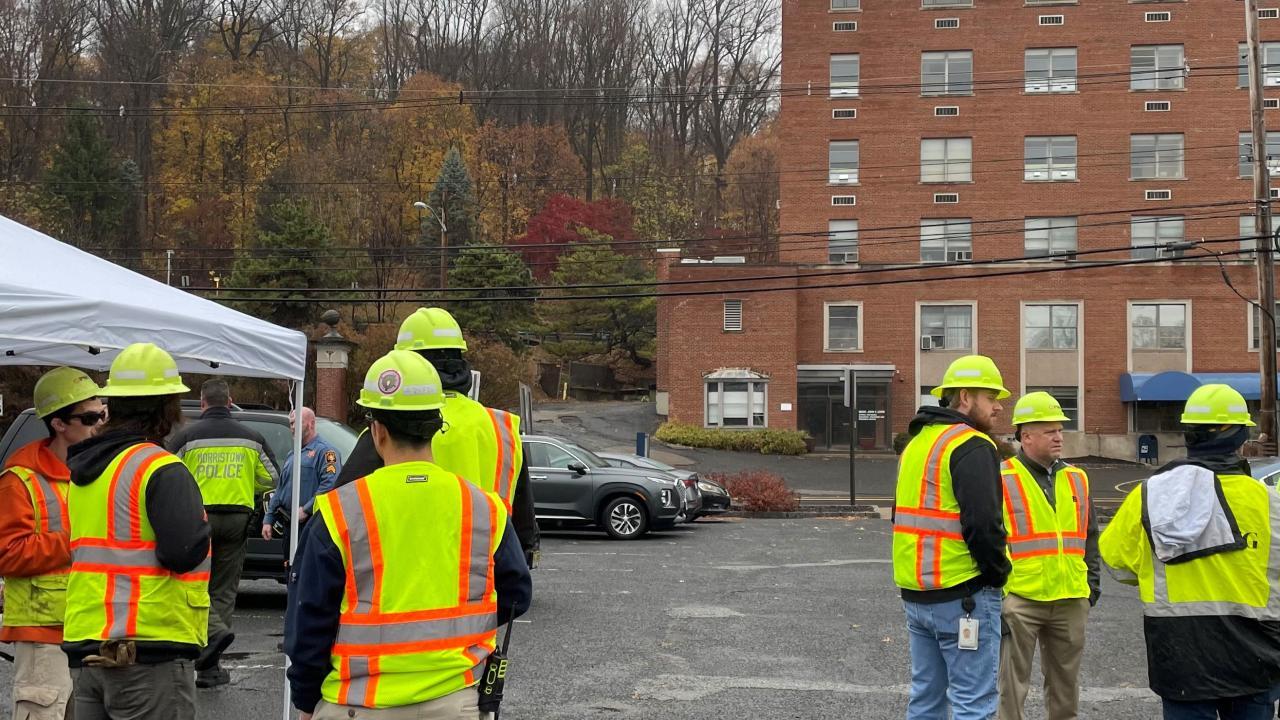 Employees standing outdise in a parking lot wearing high vis vests and hard hats.