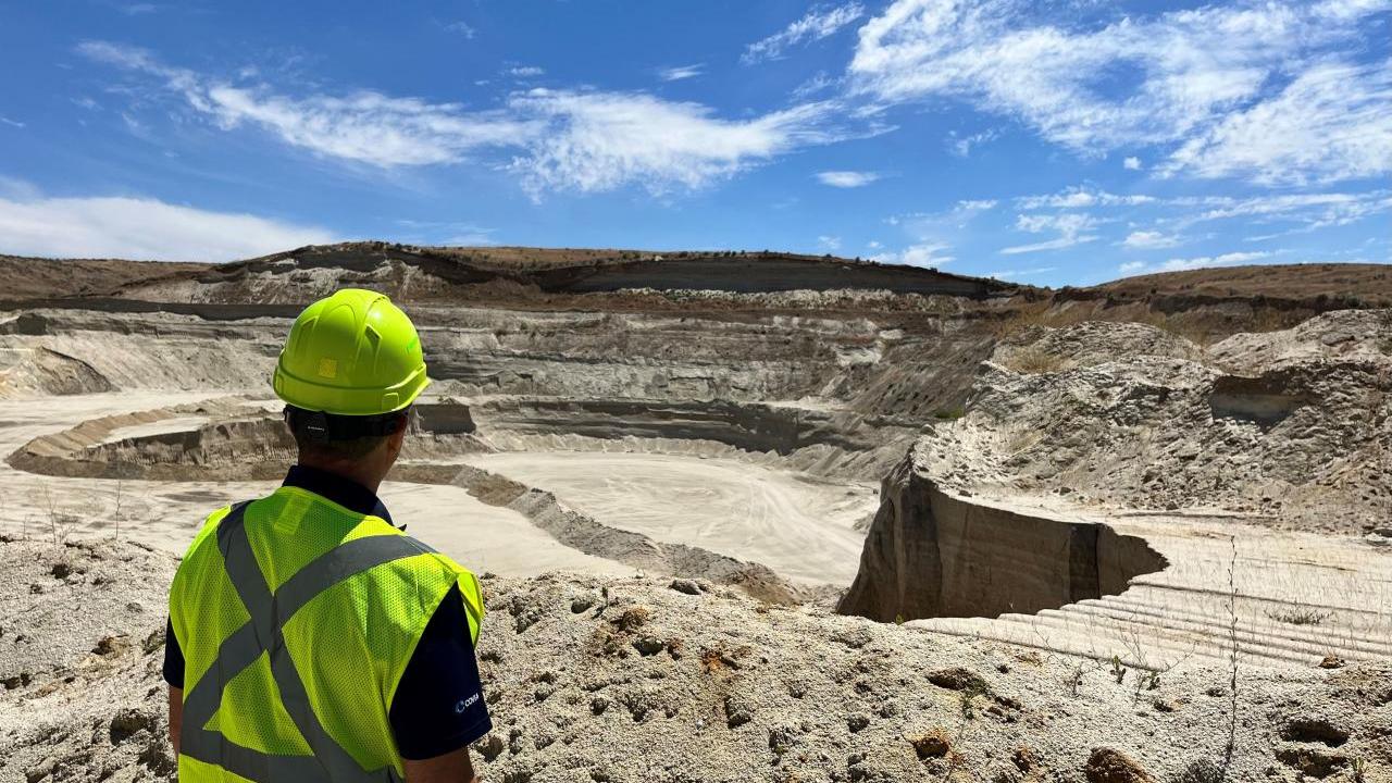 A person in a hard hat and high-vis vest looking out over a quarry area.
