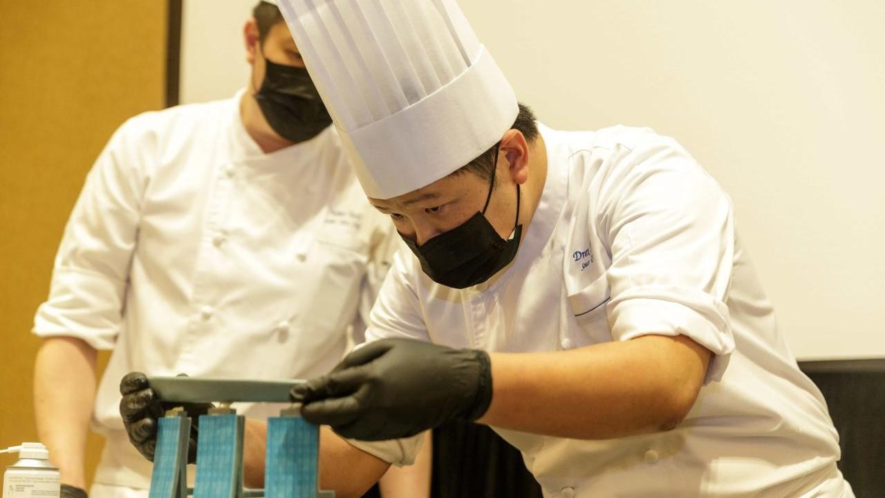 student in a chef's uniform carefully balancing a plate