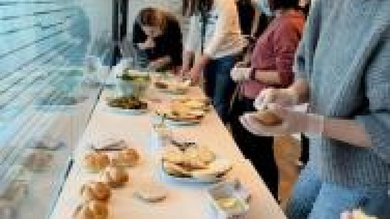 a line of people wearing protective masks making sandwiches