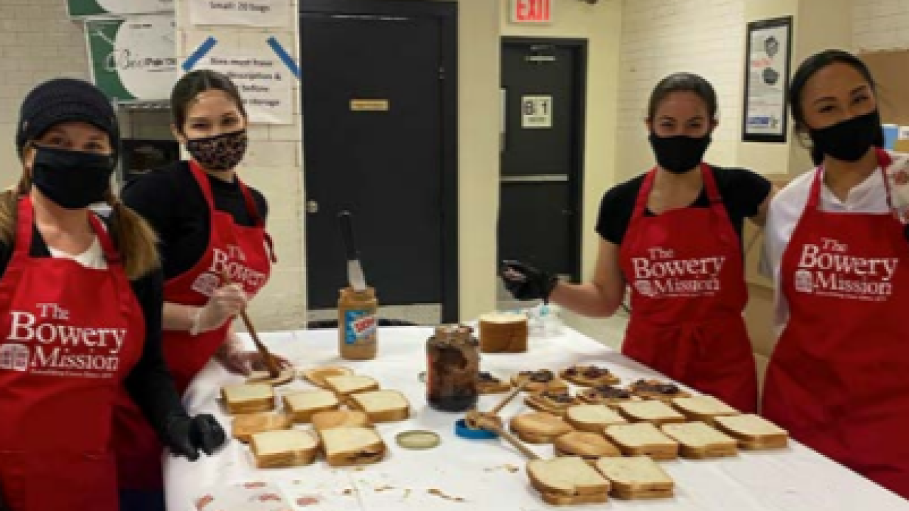 a group of four people wearing "the bowery mission" aprons, making lots of sandwiches