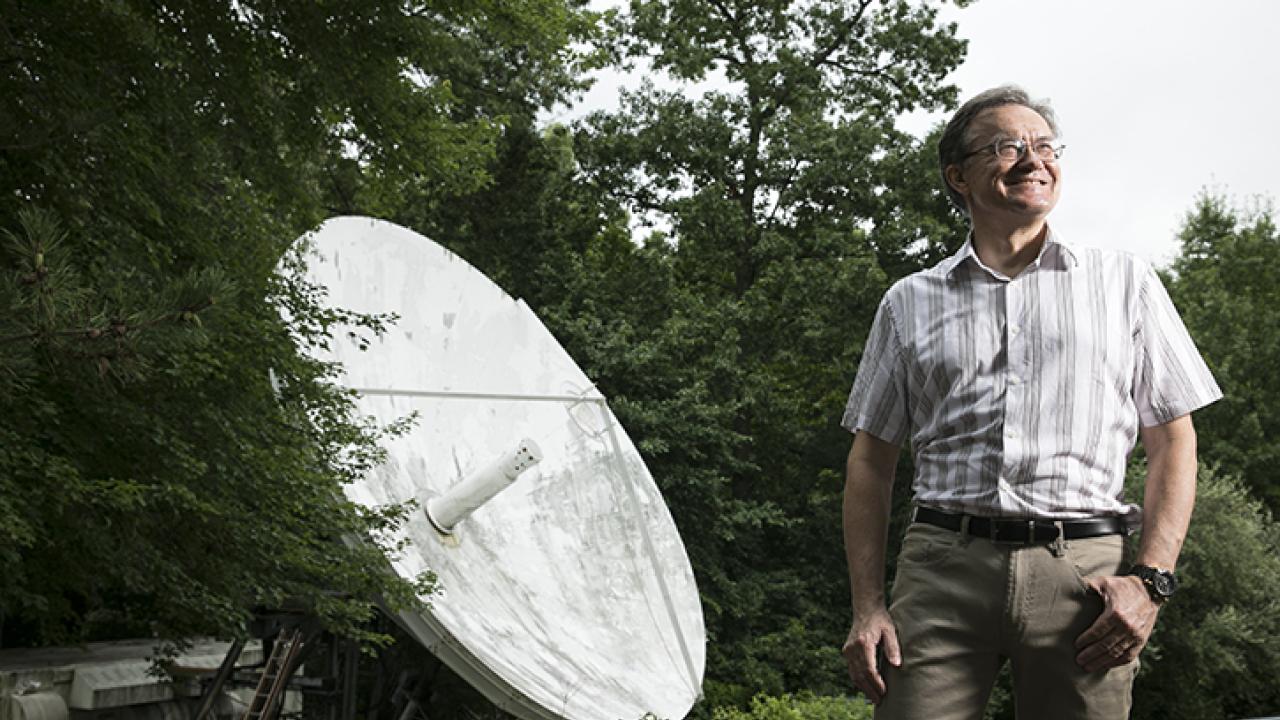 A person standing outside looking to the sky, a large satellite dish behind them